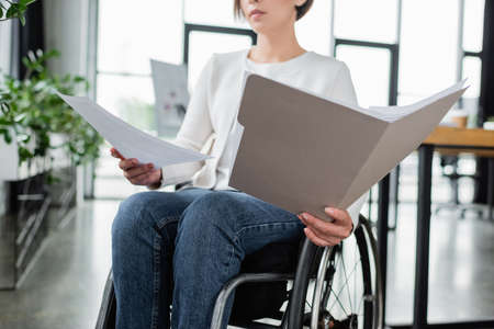 cropped view of businesswoman in wheelchair working with documents in office