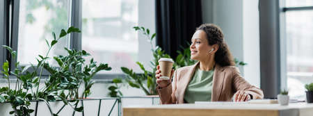 happy african american businesswoman listening music during coffee break at workplace in office, bannerの写真素材