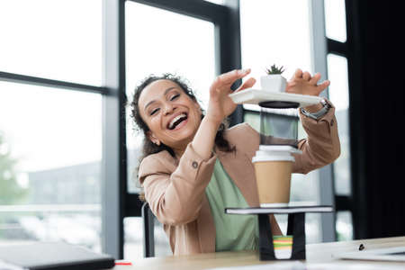 excited african american businesswoman laughing at camera while having fun at workplace in officeの写真素材