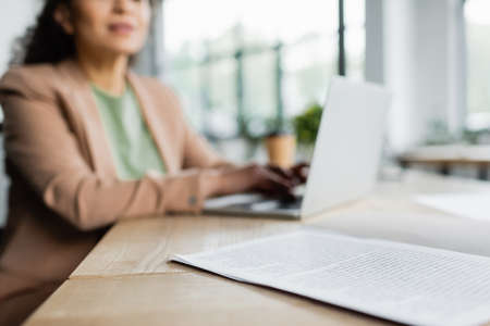 cropped view of blurred african american businesswoman typing on laptop near documents on deskの写真素材