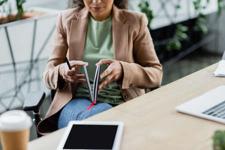 cropped view of blurred african american businesswoman opening notebook near digital tablet at workplaceの写真素材