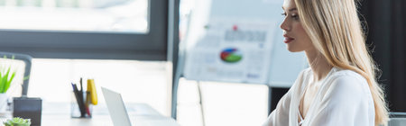 Young businesswoman looking at laptop while working in office, banner