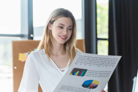 Happy businesswoman looking at blurred paper with charts in office