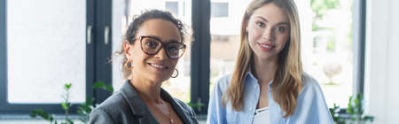 Multiethnic businesswomen smiling at camera in office, bannerの写真素材