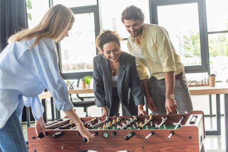 Positive interracial business people having fun while playing table soccer in officeの写真素材
