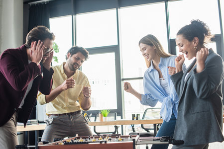 Excited multiethnic business people playing table soccer near sad colleague in officeの写真素材