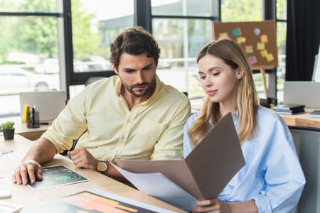 Young businesswoman holding paper folder near colleague in officeの写真素材
