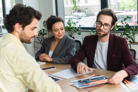 Young businessman pointing at documents near interracial colleagues in office