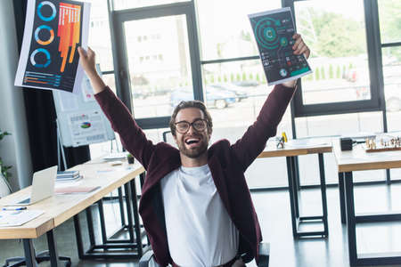 Excited businessman holding papers with graphs in officeの写真素材