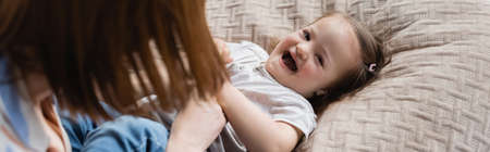 Blurred mother playing with toddler daughter with down syndrome on bed, bannerの写真素材