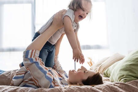 Happy woman holding excited daughter with down syndrome on bedの写真素材