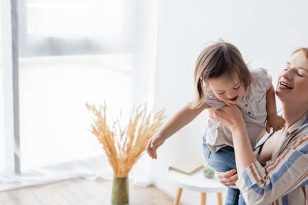 Mother holding smiling daughter with down syndrome at homeの写真素材