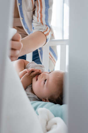 Smiling kid with down syndrome lying in baby crib near motherの写真素材