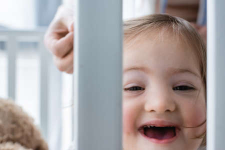 Child with down syndrome looking at camera in baby crib near blurred mother