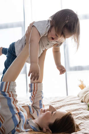 Smiling mother lifting toddler kid with down syndrome on bed