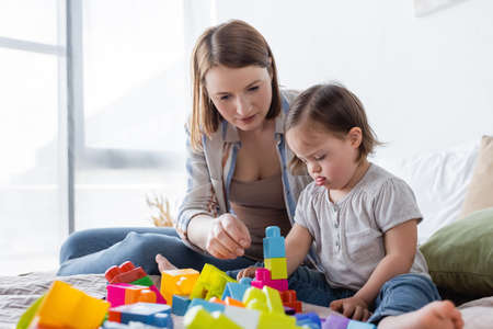 Parent and daughter with down syndrome playing building blocks on bed at home