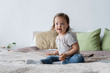 Positive child with down syndrome sitting on bed at homeの写真素材
