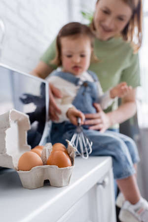 Eggs near mother and daughter on blurred background in kitchen