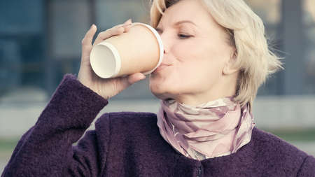 middle aged woman drinking coffee from disposable cup outdoorsの写真素材