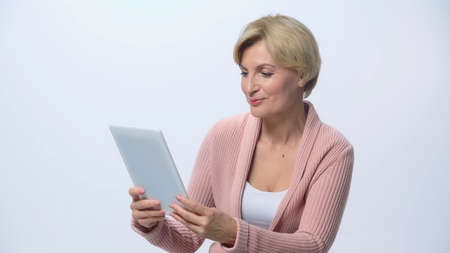 positive middle aged woman looking at digital tablet isolated on whiteの写真素材