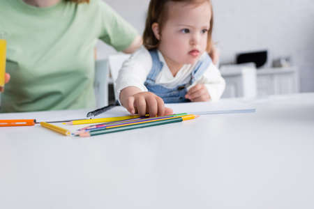 Color pencils near blurred child with down syndrome and parent in kitchenの写真素材