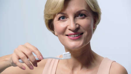 smiling middle aged woman holding toothbrush with toothpaste isolated on whiteの写真素材