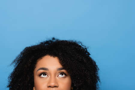 cropped view of curly african american woman looking up isolated on blueの写真素材