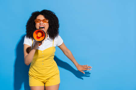 african american woman in orange eyeglasses screaming in megaphone on blue