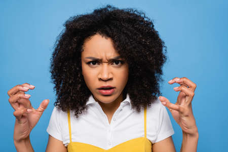 irritated african american woman showing scary gesture at camera isolated on blueの写真素材