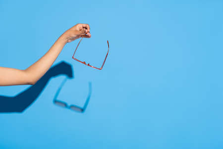 partial view of african american woman holding eyeglasses on blueの写真素材