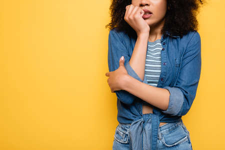 cropped view of scared african american woman holding hand near face while standing isolated on yellowの写真素材