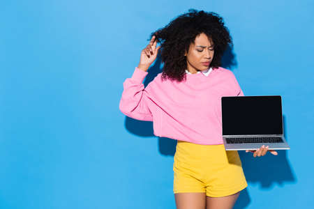 thoughtful african american woman looking at laptop with blank screen on blueの写真素材