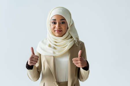 happy muslim woman in hijab showing thumbs up and smiling isolated on greyの写真素材