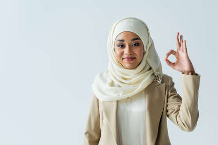 happy muslim woman in hijab showing ok sign and smiling isolated on greyの写真素材
