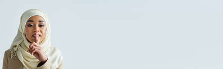 young muslim woman in hijab showing hush sign isolated on grey, bannerの写真素材