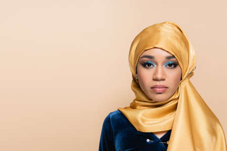 pretty muslim woman in yellow hijab looking at camera isolated on beigeの写真素材
