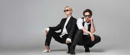 young couple in elegant suits and dark sunglasses posing on grey, bannerの写真素材