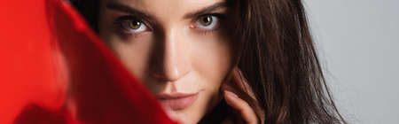 brunette young woman looking at camera near red glass isolated on grey, bannerの写真素材