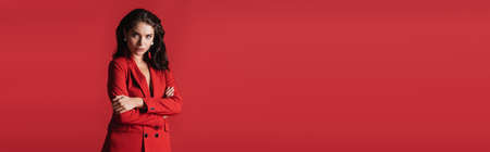 young brunette model in suit posing with crossed arms isolated on red, bannerの写真素材