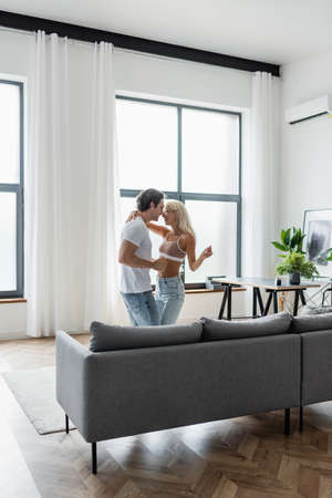 happy couple dancing near grey couch in living roomの写真素材