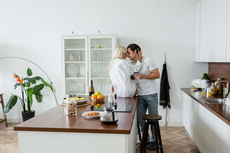 young couple with glasses of wine hugging in modern kitchenの写真素材