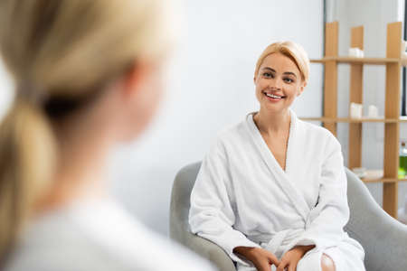happy client in bathrobe looking at blurred spa specialistの写真素材