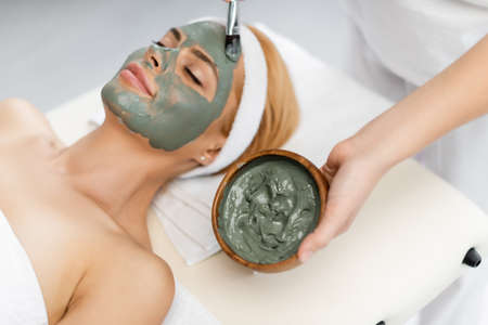 high angle view of beautician applying clay mask on face of woman lying on massage tableの写真素材