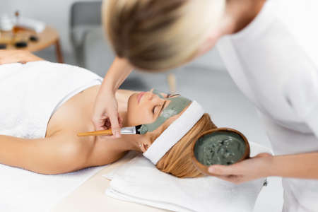 blurred beautician applying face mask on woman in spa centerの写真素材