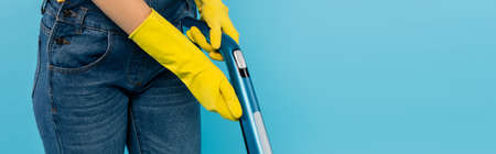 cropped view of housewife in yellow rubber gloves using vacuum cleaner isolated on blue, bannerの写真素材