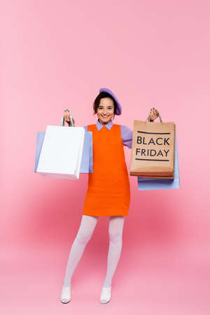 happy woman holding purchases and shopping bag with black friday lettering on pinkの写真素材