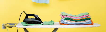 ironing board with stack of clean laundry and electric iron on yellow background, bannerの写真素材
