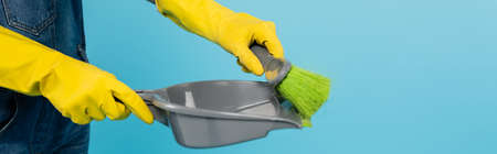 cropped view of woman in yellow rubber gloves holding scoop and broom isolated on blue, bannerの写真素材