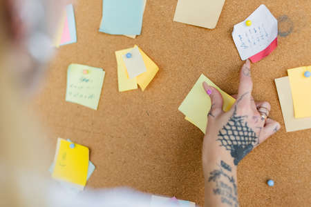 cropped view of blurred woman with tattoo near corkboard with sticky notes in officeの写真素材