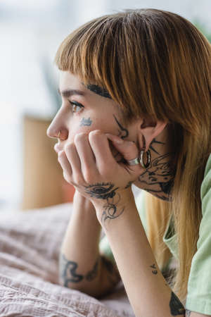 side view of tattooed woman with piercing looking away on bed at homeの写真素材